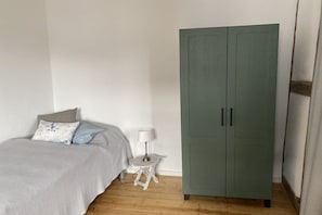 A bedroom with a bed, a small white nightstand, a lamp, and a green wardrobe. - Old nail forge Bremm (Bremm)