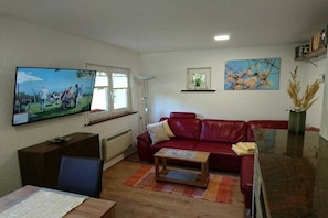 Ein Wohnzimmer mit einem roten Sofa, einem Holztisch, einem Fernseher an der Wand und einem kleinen Fenster.