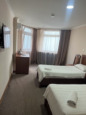 A hotel room with two beds, a desk, a chair, a TV, and a window with curtains. - Hotel Bakuri (Batumi)