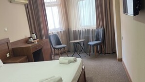 Een hotelkamer met een bed, een bureau, een stoel, een televisie en een raam met gordijnen.