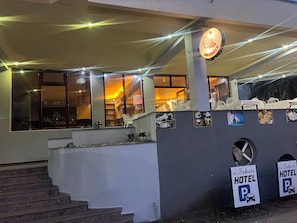 Entrada de hotel con una escalera, un letrero que indica un área de estacionamiento y un letrero con un logotipo.