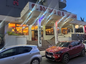 A hotel entrance with a staircase leading to the lobby, a sign indicating the hotel name, and a red car parked in front. - Hotel Bakuri (Batumi)