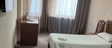 A hotel room with two beds, a desk, a chair, a television, and a window with curtains.