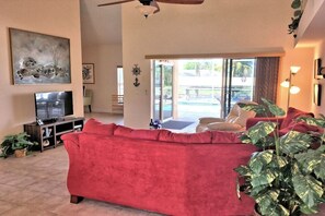 A living room with a red sofa, a television, a ceiling fan, and a large plant. - Holiday home with 1 bedroom (Cape Coral)