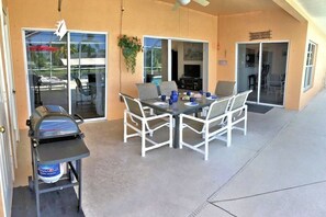 Une terrasse extérieure avec une table et des chaises, un barbecue et un ventilateur de plafond.