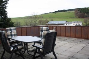 Une terrasse extérieure avec une table ronde et quatre chaises, une clôture en bois et une vue sur une maison et des champs.