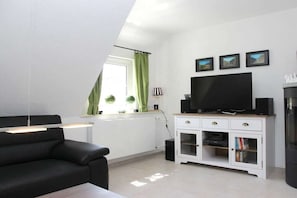 A modern living room with a black sofa, a TV on a white cabinet, and a window with green curtains. - Holiday home Olsberg (Olsberg)
