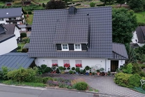 A white house with a grey tiled roof, a front garden with potted plants, and a visible number '12' on the house. - Holiday home Olsberg (Olsberg)