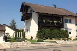 Ein zweistöckiges Haus mit Balkon, einer Steinsichtmauer und einem gepflegten Garten.