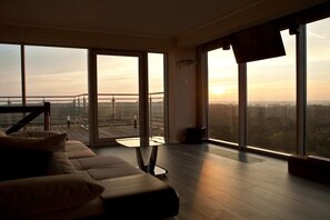 Una sala de estar moderna con un sofá, una mesa de centro de vidrio y grandes ventanales con vistas a la ciudad.