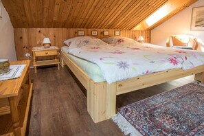 Ein Zimmer mit Holzwänden, einem Bett, Nachttischen, einem Sessel und einem Teppich.