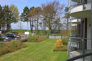 Een woongebouw met balkon, parkeerplaats en gazon met bomen.