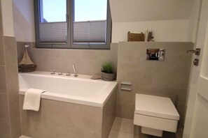 A bathroom with a bathtub, toilet, and a window.