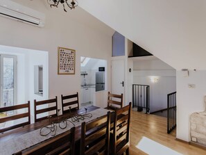 Un espace repas avec une table et des chaises en bois, une cuisine à l’arrière-plan et un escalier menant à un niveau supérieur.