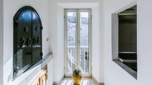 Un couloir avec une grande porte métallique portant l’inscription « 2006 », une porte vitrée donnant sur l’extérieur et un pot de fleurs posé sur le sol.