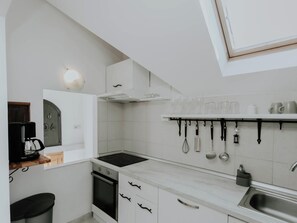 Une cuisine moderne avec des meubles blancs, une cuisinière encastrée, une machine à café et un porte-ustensiles suspendu.