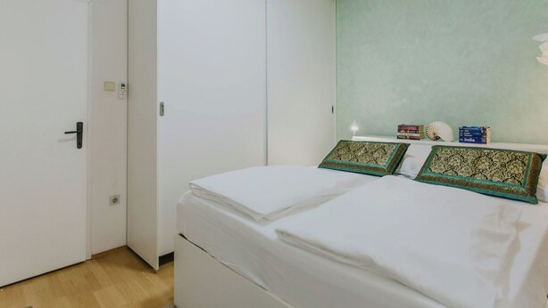 Une chambre à coucher comprenant un lit, une armoire, une table de chevet avec des livres et un climatiseur fixé au mur.