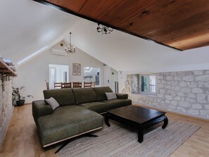 A loft-style living room with a green sectional sofa, a dark wooden coffee table, and a stone accent wall. - Vacation home Nerium by Interhome (Trogir)