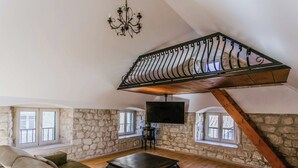 Une pièce de style « loft », avec des murs en pierre, un plafond en bois, un grand canapé, une table basse et un téléviseur fixé au mur.