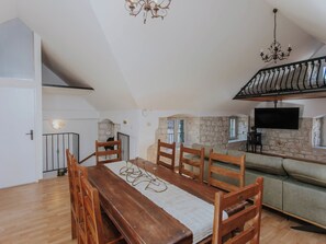 A dining area with a wooden table and chairs, a stone wall, a TV mounted on the wall, and a staircase with a railing. - Vacation home Nerium by Interhome (Trogir)