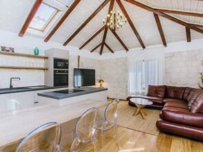 Cozinha moderna com forno embutido, televisão de tela plana e área de refeições com mesa e cadeiras de vidro.