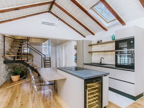 A modern kitchen with a built-in oven, a dining area with a wooden table and chairs, a stone wall, and a staircase with a wooden railing. - Apartment Nerium by Interhome (Trogir)