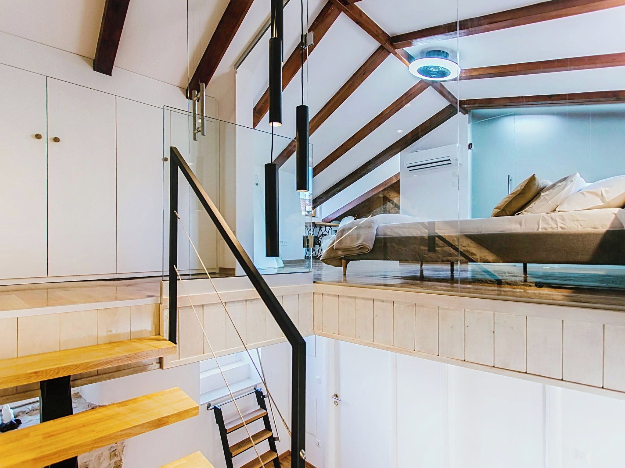 Ein kleiner Raum mit Etagenbett, Treppe und Deckenventilator.