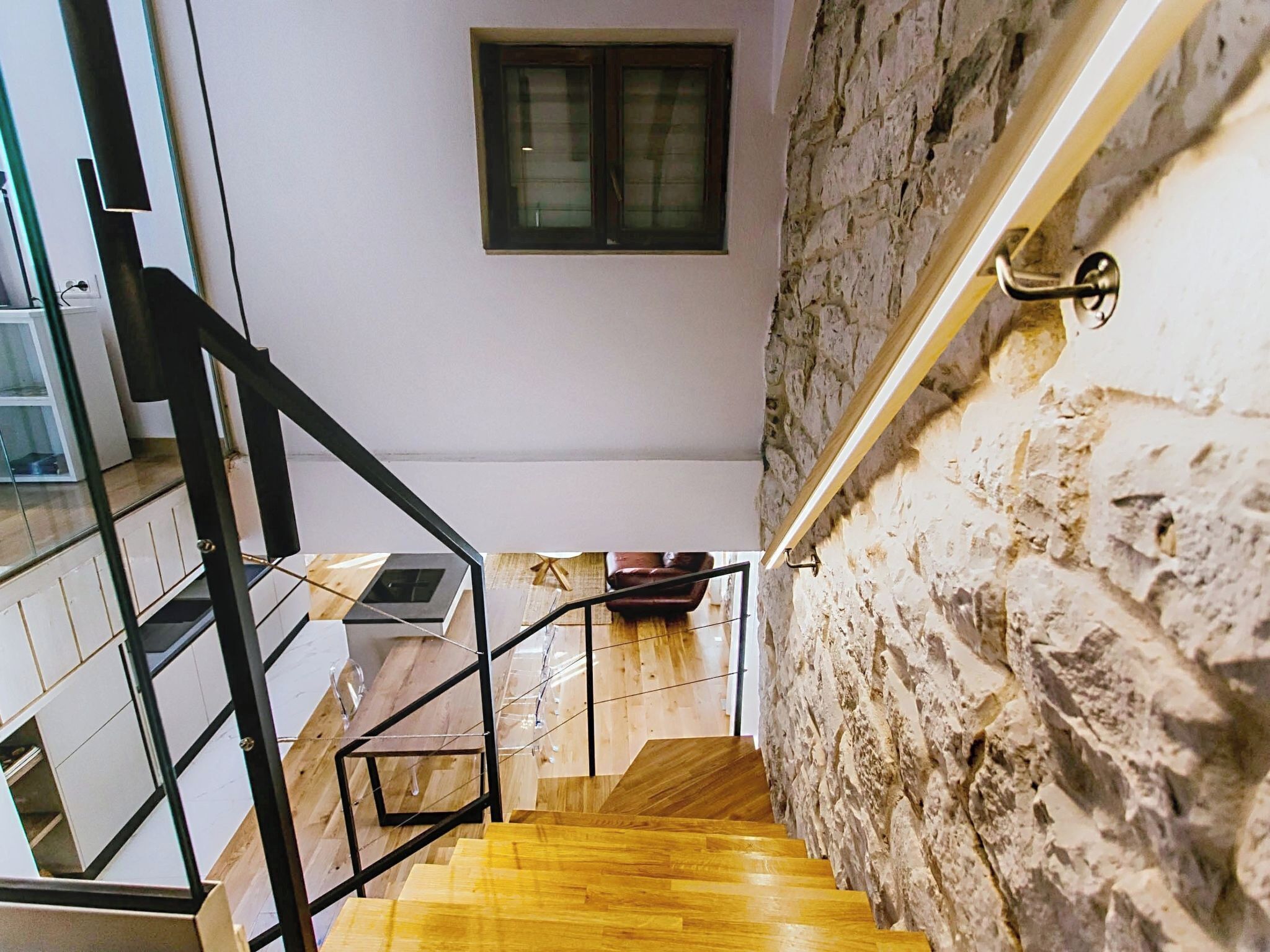 Eine Treppe mit Holzstufen und Metallgeländern, die zu einem Raum mit einer Steinwand und einem Fenster führt.