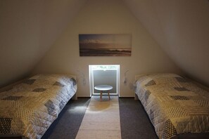 Ein Zimmer mit zwei Betten, einem kleinen Tisch, einem Fenster mit Jalousien und einem Bild an der Wand.