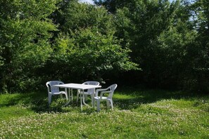 Ein Set aus weißem Plastiktisch und -stühlen in einer grünen Wiese, im Hintergrund Bäume.
