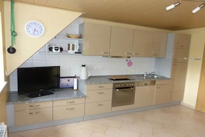 Una cucina con mobili color beige, un forno a microonde, una macchina da caffè, un tostapane e una sveglia appesa al muro.
