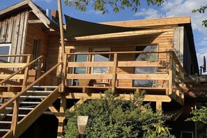 Eine Holzhütte mit einem Balkon, einer Treppe und einem Fenster mit Blick auf einen Garten.
