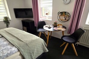 Hotelkamer met een bed, een televisie, een tafeltje met een vaas, stoelen en een raam met gordijnen.