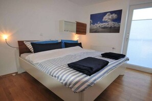 Ein Schlafzimmer mit einem Bett, einem Nachttisch, einem Wandregal und einem Fenster mit Jalousien.