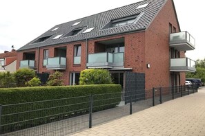 Ein modernes Wohngebäude mit zwei Etagen, Ziegelaußenwand, mehreren Balkonen und einem gepflasterten Weg.