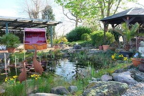 Ein Garten mit Teich, Steinen und Kübelpflanzen.