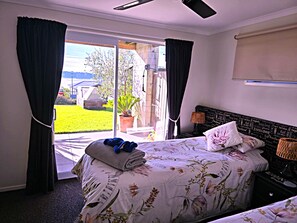 A bedroom with a bed, a nightstand, a lamp, and a view of the outdoors. - Omokoroa Sea View Apartment, stunning views, amazing sun rises, quiet spot (Ōmokoroa)