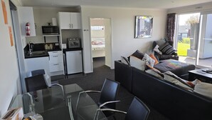 A compact room with a kitchenette, a bed, a sofa, a glass dining table, and a view of the outdoors. - Omokoroa Sea View Apartment, stunning views, amazing sun rises, quiet spot (Ōmokoroa)