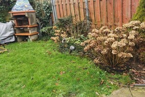 En have med en murstensgrill, et træhegn og mange forskellige planter.