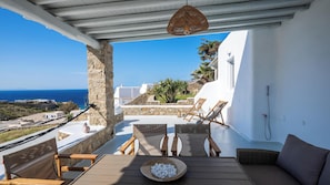 A terrace with a view of the sea, stone walls, white buildings, and outdoor furniture. - Cavo Blue Villas, Luxury villa with Pool and Aegean View (Elia)