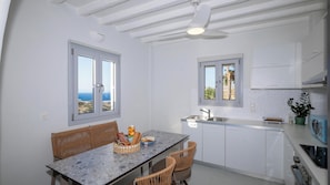 A kitchen with a view of the sea, a dining area with wicker chairs, and a ceiling fan. - Cavo Blue Villas, Luxury villa with Pool and Aegean View (Elia)