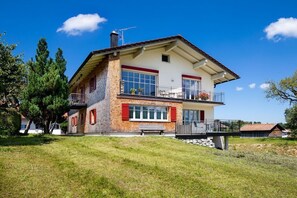 Una casa de dos pisos con balcón, chimenea y patio cubierto de césped.