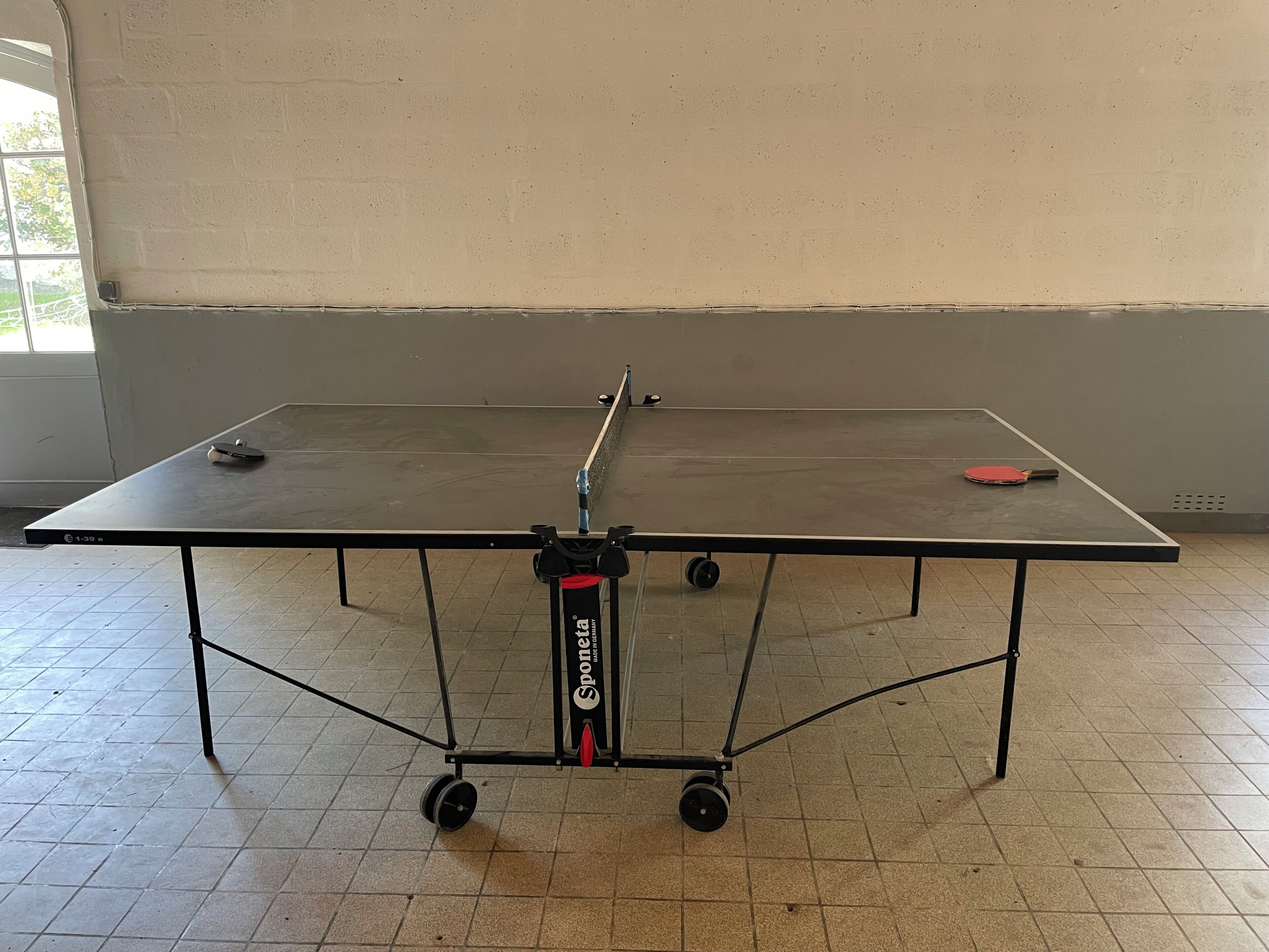A ping pong table with wheels, a net, and two paddles.