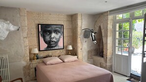 Un dormitorio con cama, dos lámparas de noche, una silla de estampado de cebra, pared de piedra, escultura de cabeza de cebra montada en la pared y un ventanal grande.