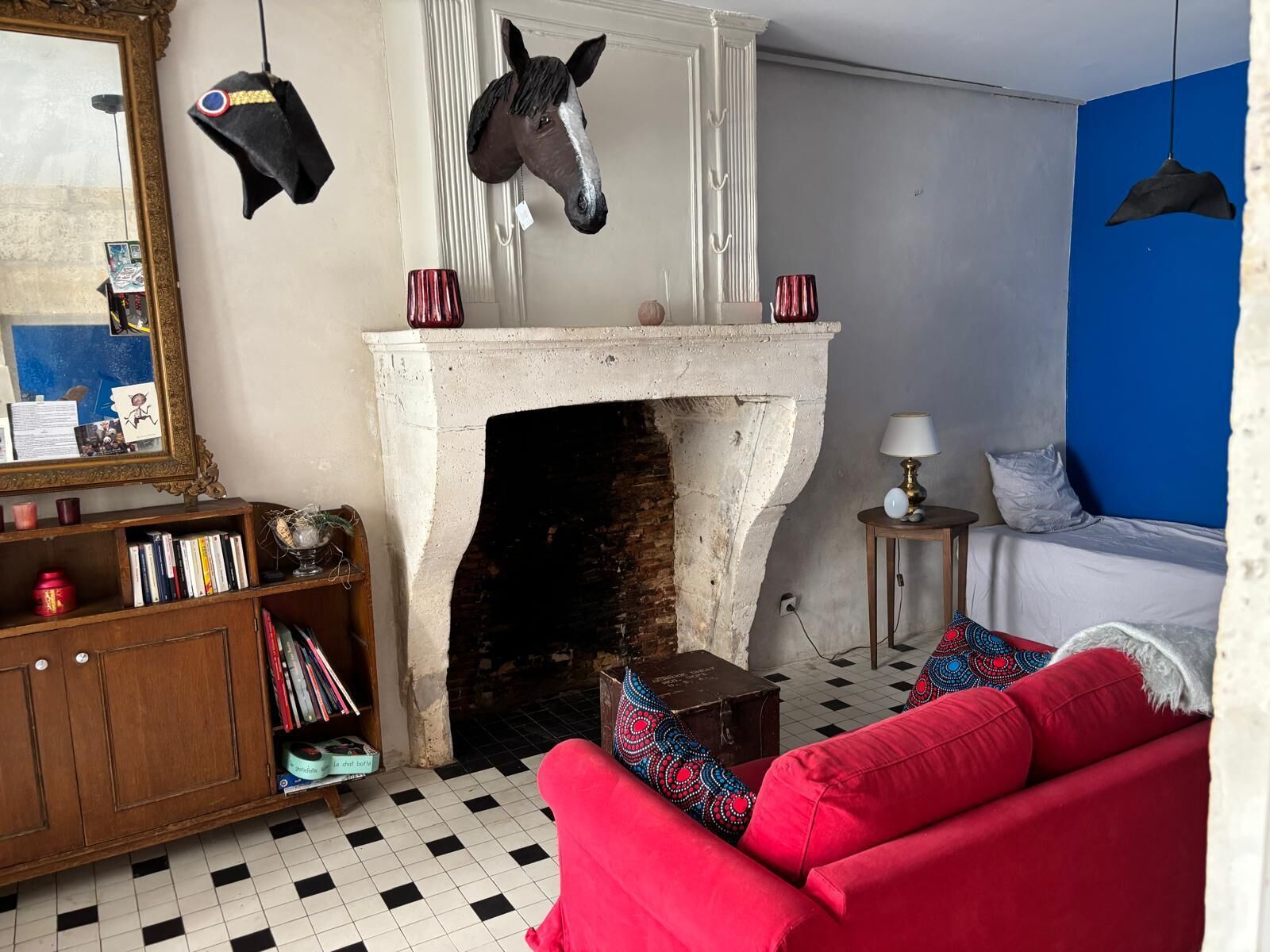 A room with a fireplace, a red sofa, a bookshelf, and a hanging horse head decoration.
