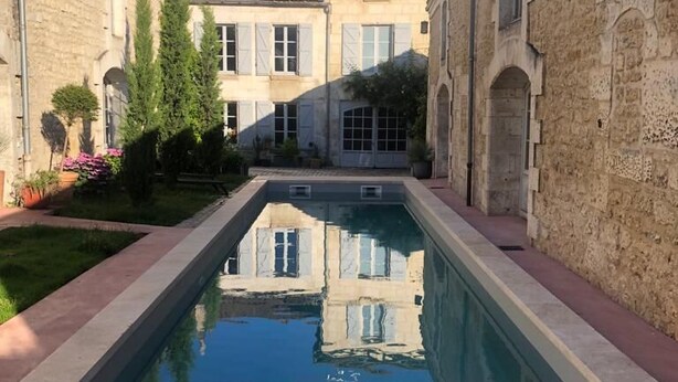 Un patio con piscina, edificios de piedra y cielo despejado.