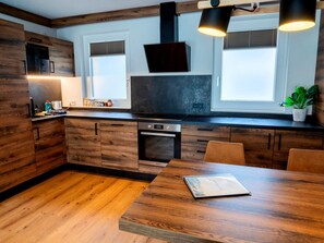 A modern kitchen with wooden cabinetry, a built-in oven, and a dining area with a wooden table. - Comfortable Suite for 4 Guests (Rauris)