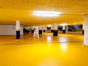 A parking garage with yellow floors, white pillars with blue bases, and a large mural on the far wall. - Comfortable Suite for 4 Guests (Rauris)