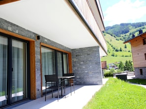 Un bâtiment moderne doté de grandes portes vitrées, d’un mur en pierre et offrant une vue sur des collines verdoyantes.