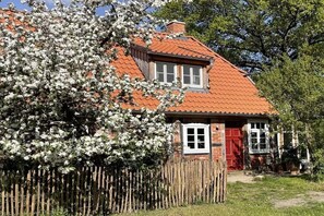 A traditional house with a red-tiled roof, a wooden fence, and a blooming tree. - Old Elbe boatman's house (Unbesandten)